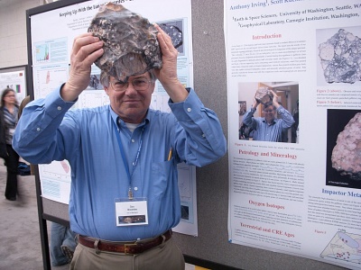 Dr. Brownlee holding Northwest Africa 5000 replica in front of poster